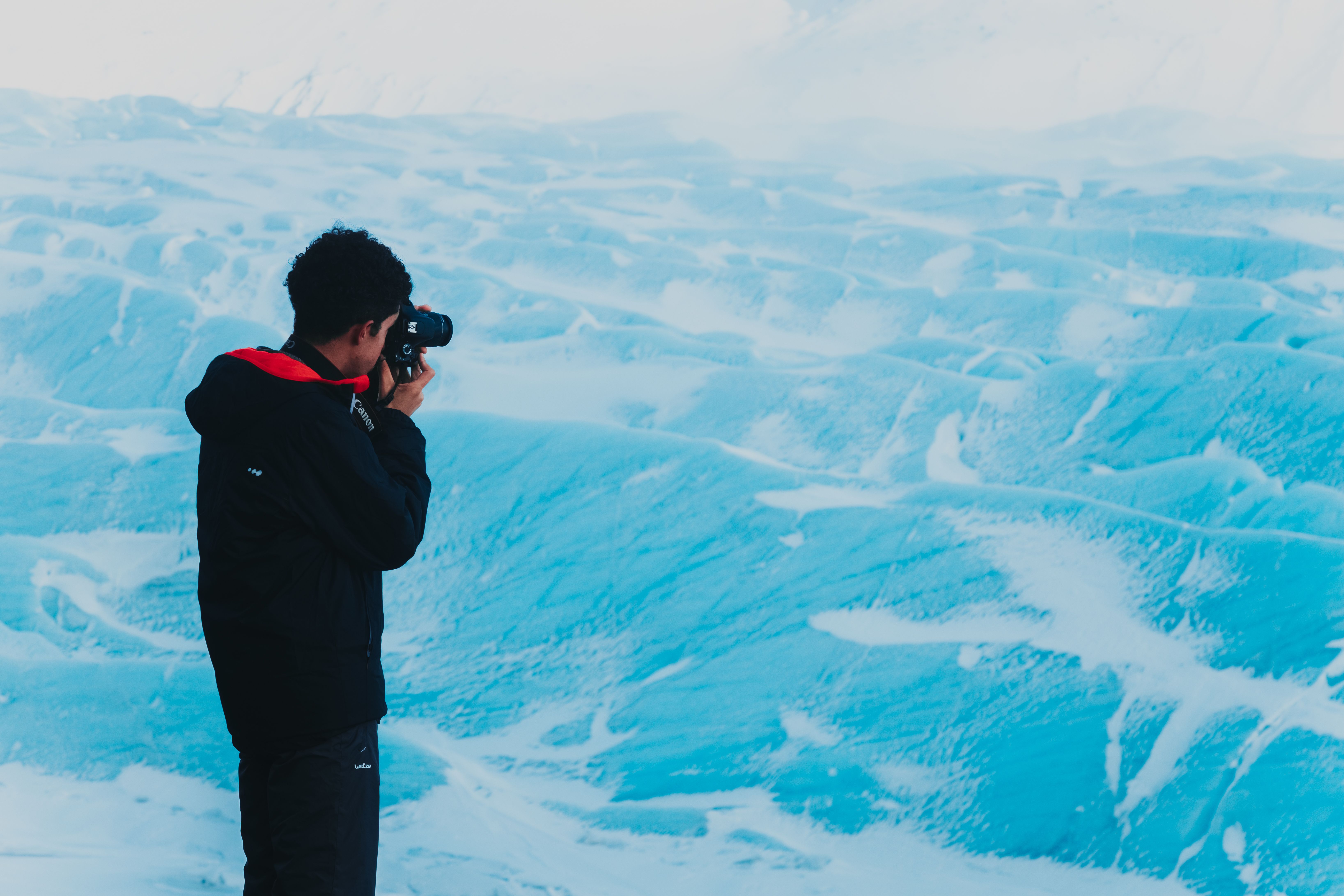 Back view of male photographer in warm jacket standing on high viewpoint and photographing amazing mountains in winter time