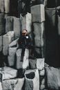 Full body male in warm winter clothes sitting on edge of basalt column of amazing natural formation in nature