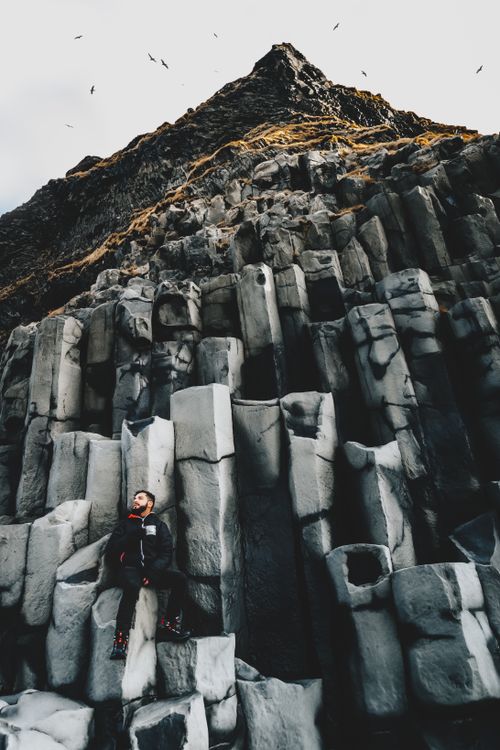 Free From below of hiker sitting on high stone columns on remote Nordic shoreline Stock Photo