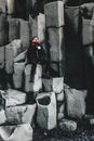 Inspired tourist in winter clothes sitting on basalt columns on cold seashore and looking away