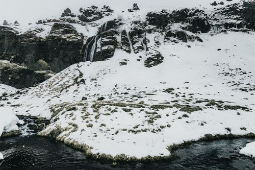 Free Peaceful water flowing alongside cold coast covered with snow against rocky cliffs in gloomy day Stock Photo