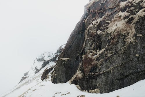 Rough boulder of remote mountain covered with white snow in misty cold valley