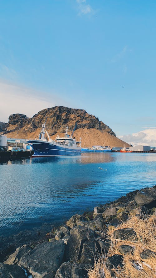 Port with moored boats in calm peaceful water with rocky coast in clear sunny day