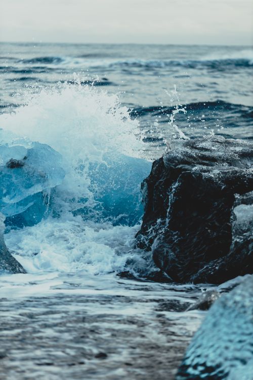 Free Powerful cold waves of ocean dashing against rock with glaciers flowing around in daylight Stock Photo