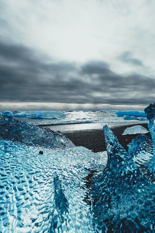 Free Majestic clear ice chunks on coast with splashing waves of ocean under cloudy sky in sunlight Stock Photo