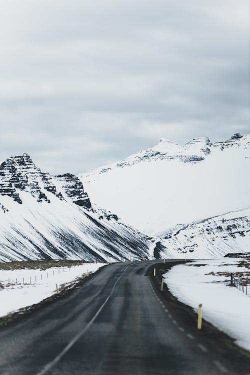 Perspective asphalt road running away through cold rocky mountains and fields in gloomy day