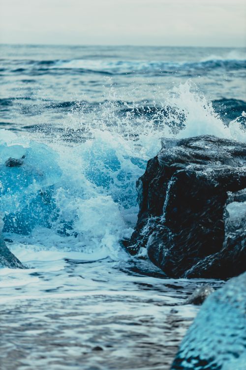 Free Splashing crystal blue waves of ocean dashing against rocky cliff and ice in water Stock Photo