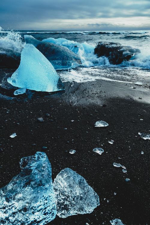 Free Wild coastline with black volcanic sand and ice against powerful splashing waves of ocean Stock Photo