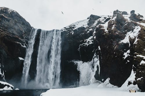 Scenery view of rapid cascade with foamy water flow in rough mounts near pond in winter