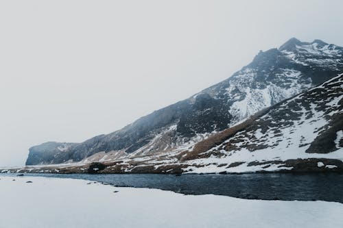 Scenery view of rough mountains covered with snow near rippled river under white sky