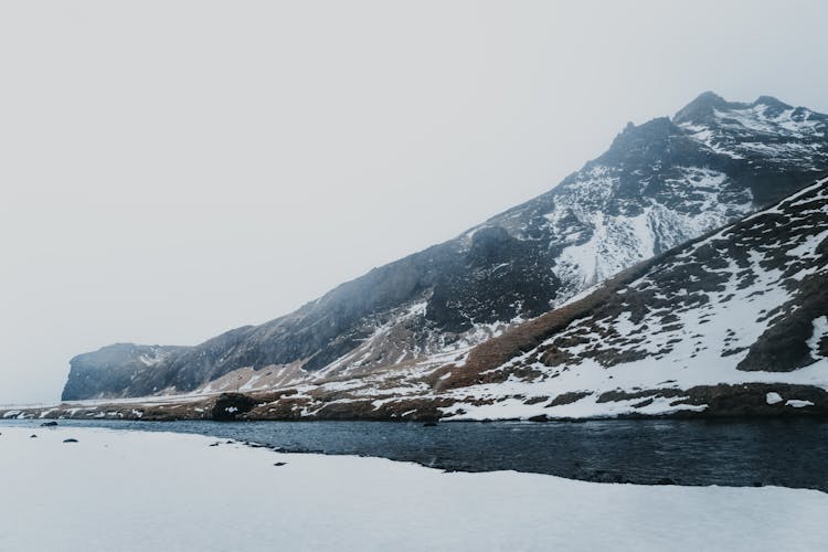 Snowy Ridge Near River Under Sky In Winter