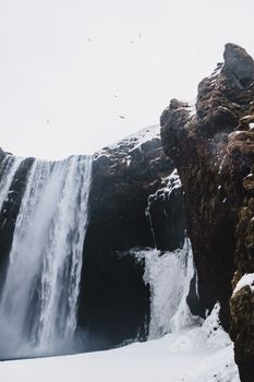从下方俯瞰，瀑布飞泻，雪地近在眼前，鸟儿在白色的天空下飞翔