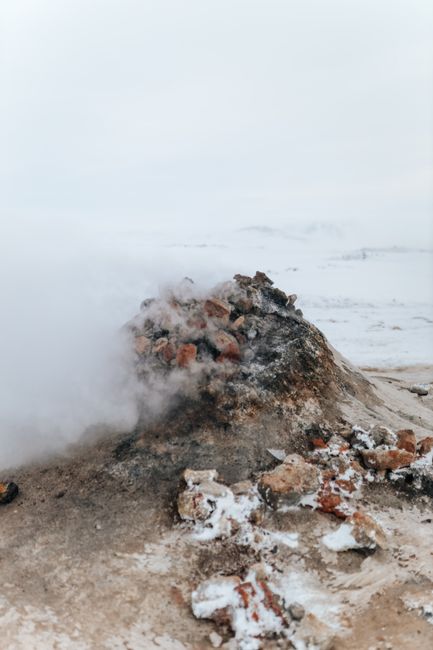 From above of rough snowy rocky formation on coast behind wavy stormy sea in mist under sky