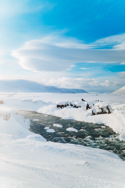 Free Breathtaking view of rapid creek fluid between snowy mountains under blue cloudy sky in winter in fog Stock Photo