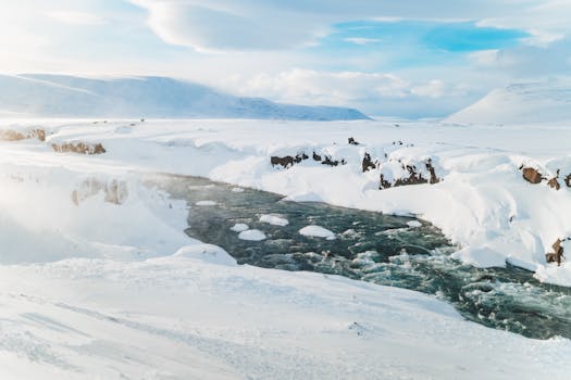 Picturesque view of river flow between snowy mounts under blue cloudy sky in winter in fog