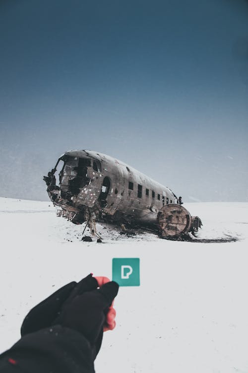 Crop unrecognizable person demonstrating small sticker with letter P against ruined plane after accident on snowy land under sky