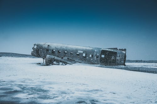 Free Aged ruined airplane after accident on snowy land behind mounts under sky in winter Stock Photo
