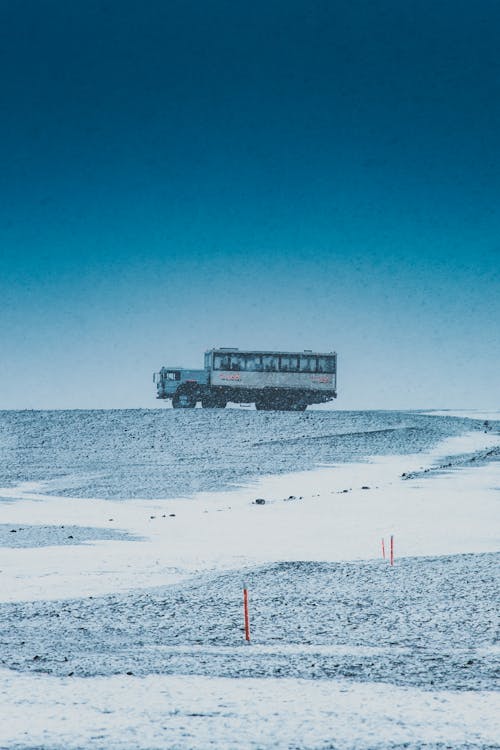 Aged vehicle with unrecognizable passengers driving on snowy mount under sky in winter