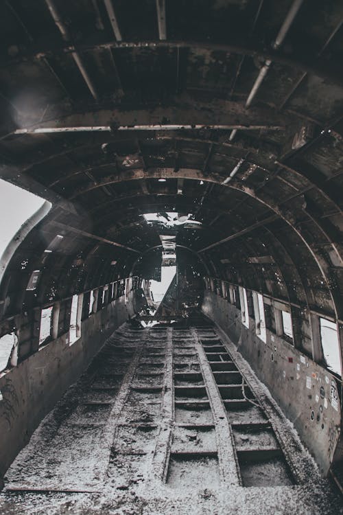 Black and white of aged abandoned aircraft cabin with rough floor and weathered ceiling after disaster