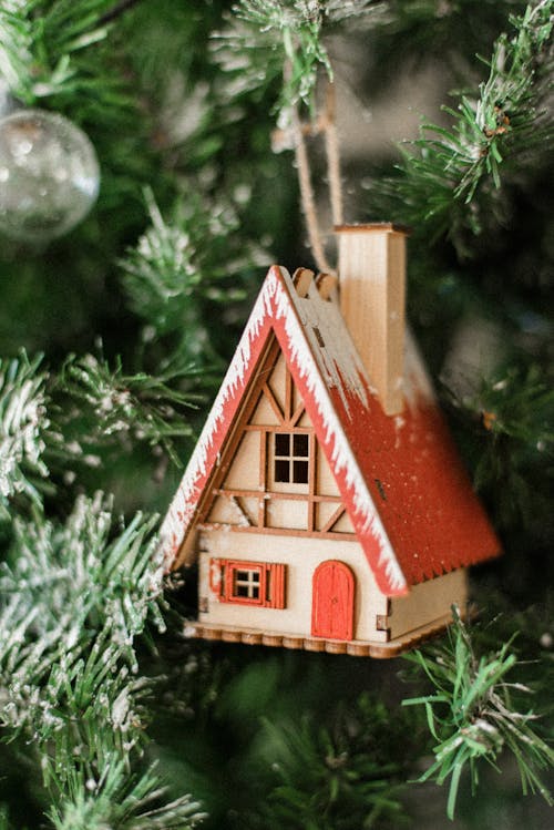 Cute wooden toy house hanging on decorated artificial Christmas tree during festive season in December
