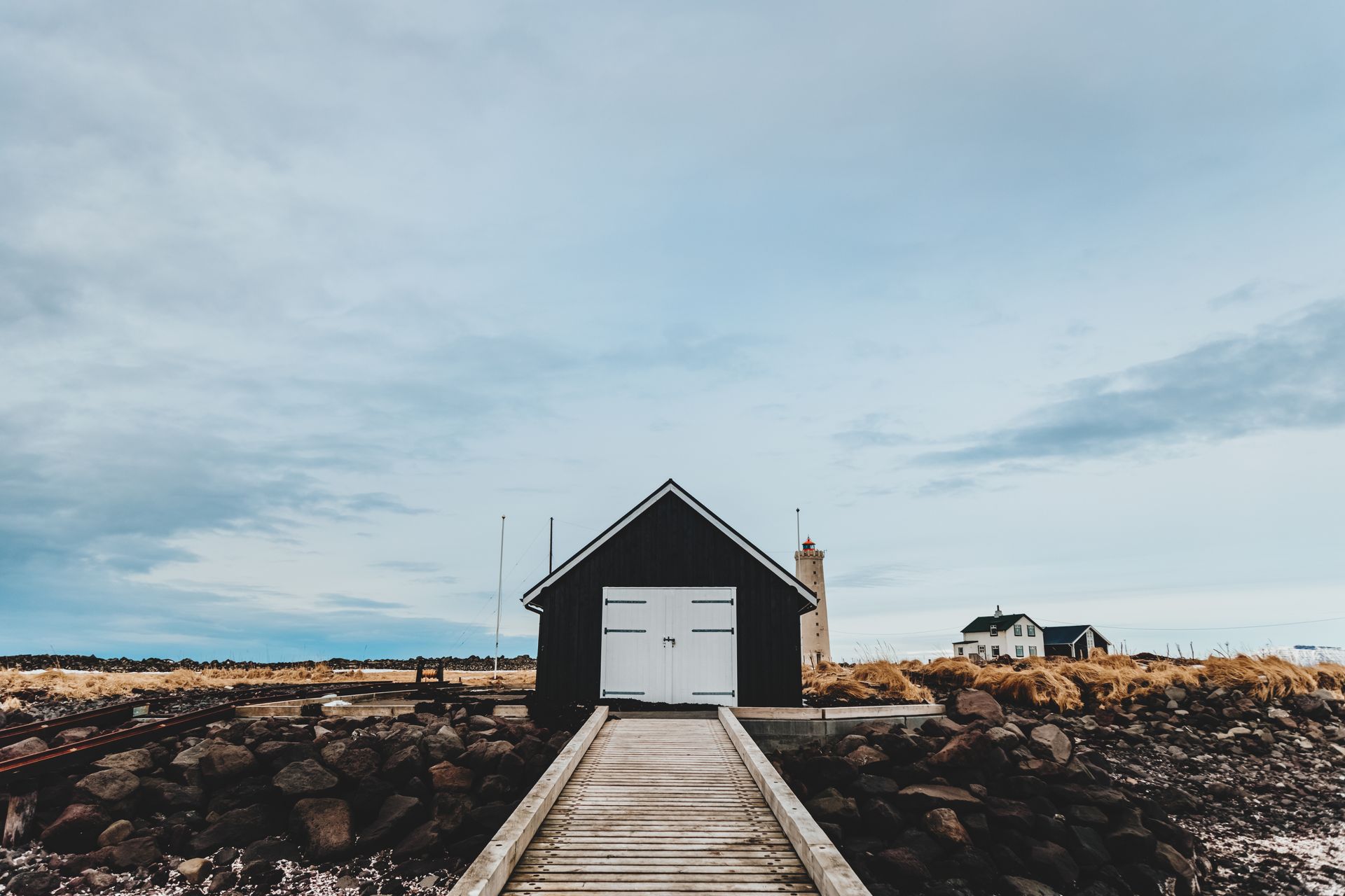 Narrow wooden pier leading to old house on stones with snow under sky in daylight