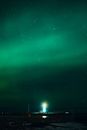 Beacon with glowing rays under colorful green sky with northern lights at dusk