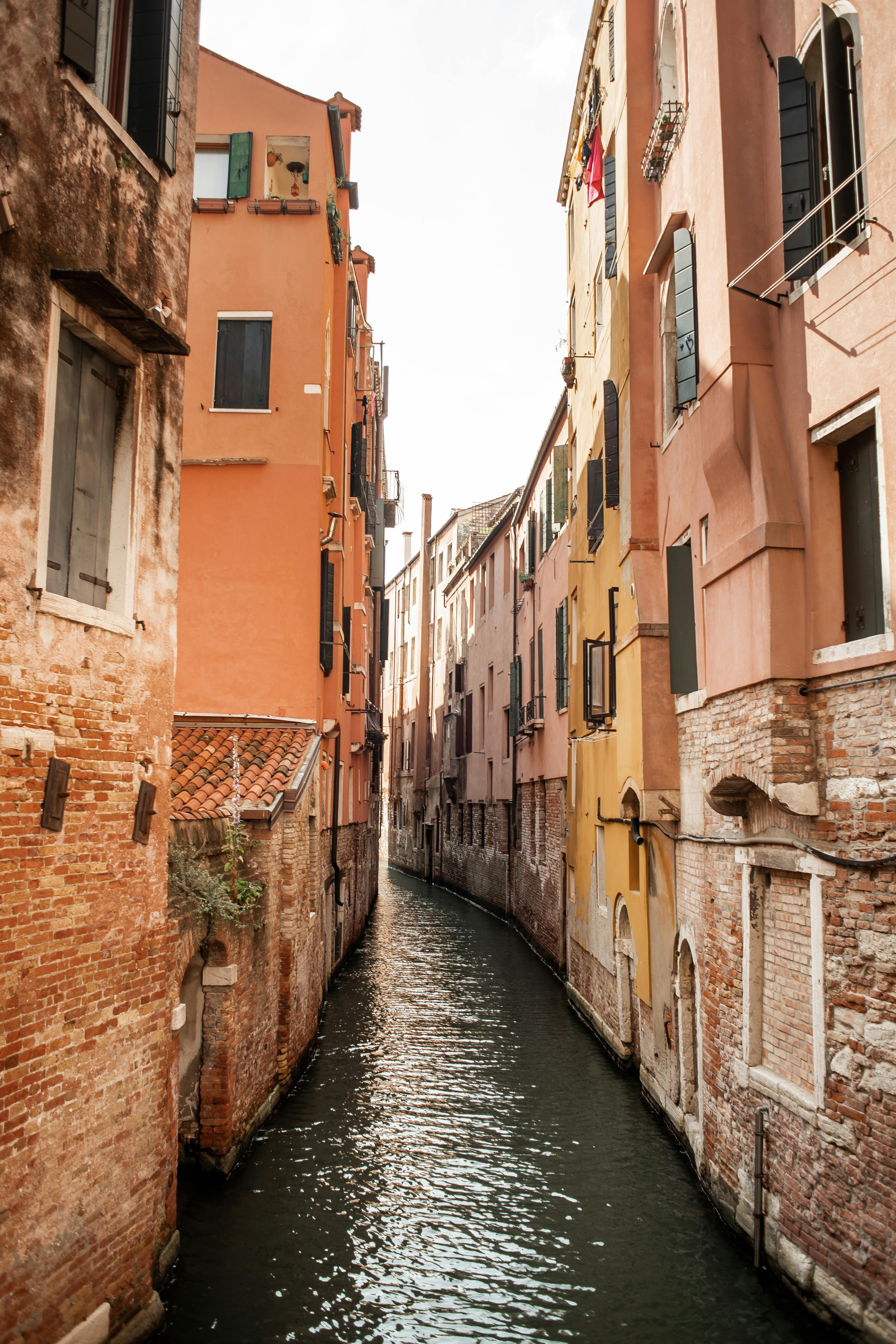 Historical ancient buildings with cute windows located near empty city canal in Venice on sunny day
