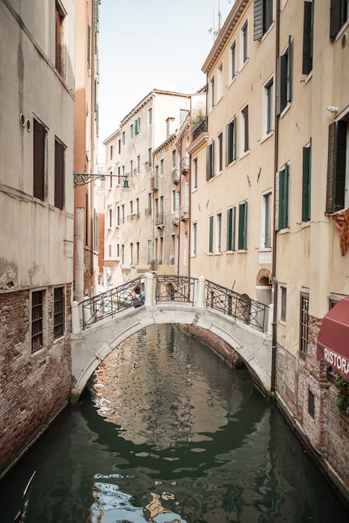 Beautiful narrow Venice canal flowing along medieval old buildings connected by cute wite bridge in daylight