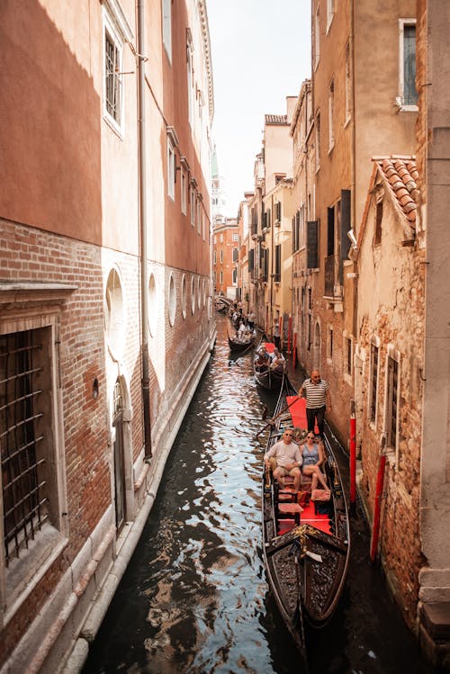 Beautiful narrow Venice canal with gondolas and tourist floating near shabby brick historical buildings with cute windows of different sizes and shapes