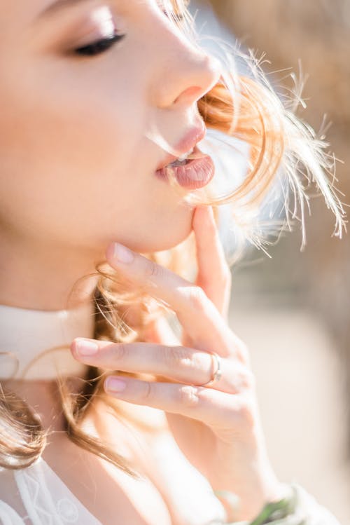 Free Side view crop gorgeous young lady in back lit standing against bright sun with eyes closed and gently touching chin sensually Stock Photo