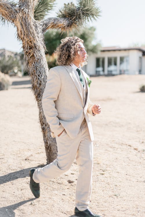 Positive groom in stylish white suit in arid area