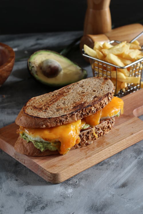 Free From above of yummy sandwich with crispy bread loafs and bright cheddar cheese near avocado and French fries Stock Photo