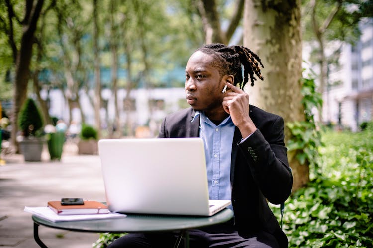 Pensive Black Businessman With Earbuds And Laptop In Park