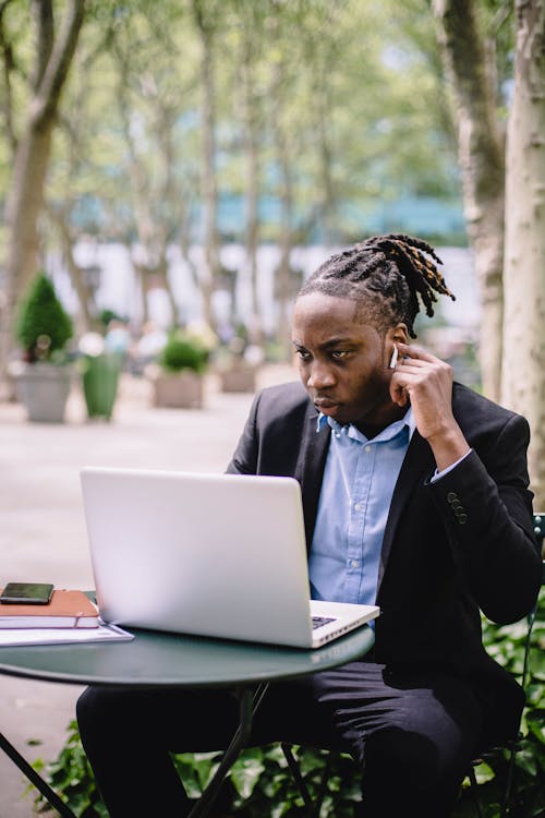 Free Thoughtful black man in TWS earphones using laptop during work in cafe Stock Photo