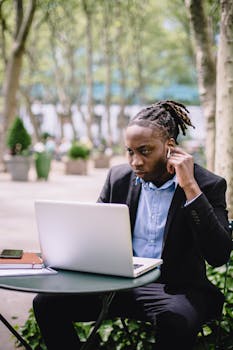 Young man in suit working on laptop outdoors, focused and professional.
