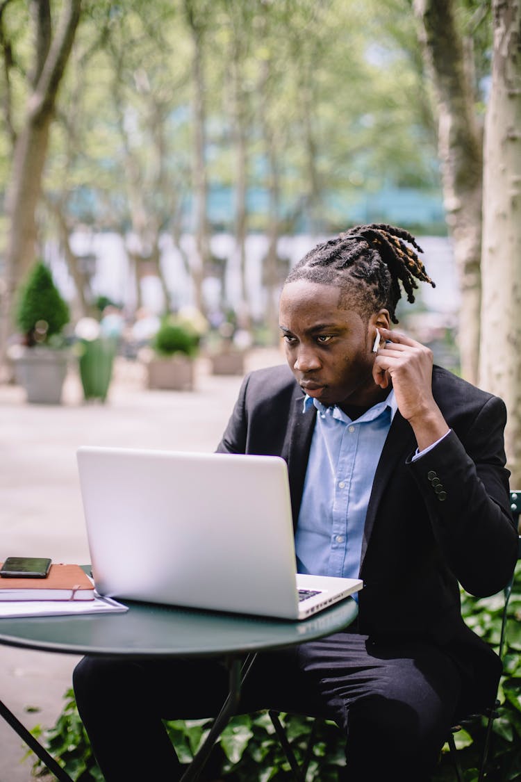 Thoughtful Black Man In TWS Earphones Using Laptop During Work In Cafe