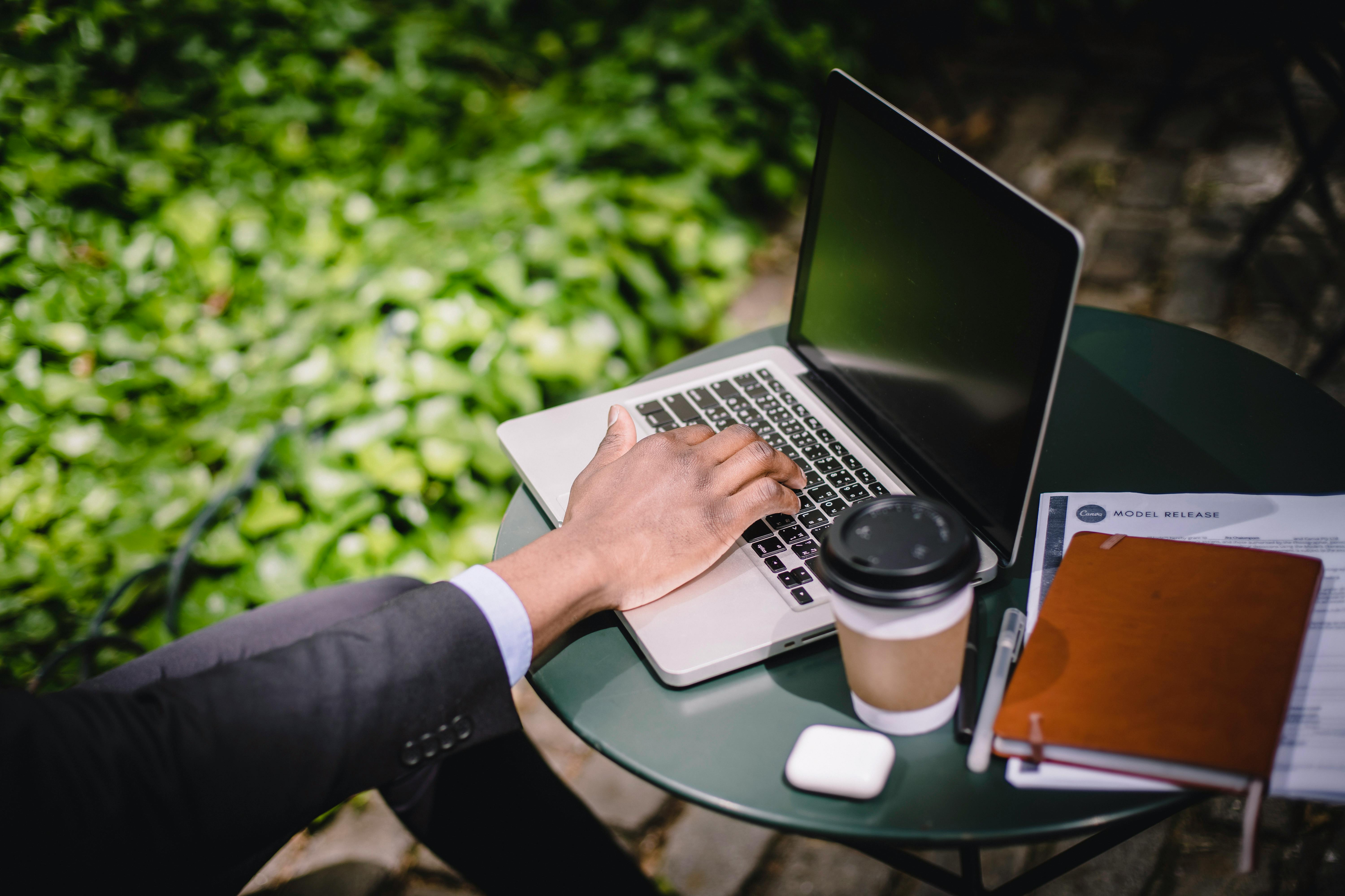 Free Crop male freelancer working on laptop in street cafe on sunny day Stock Photo