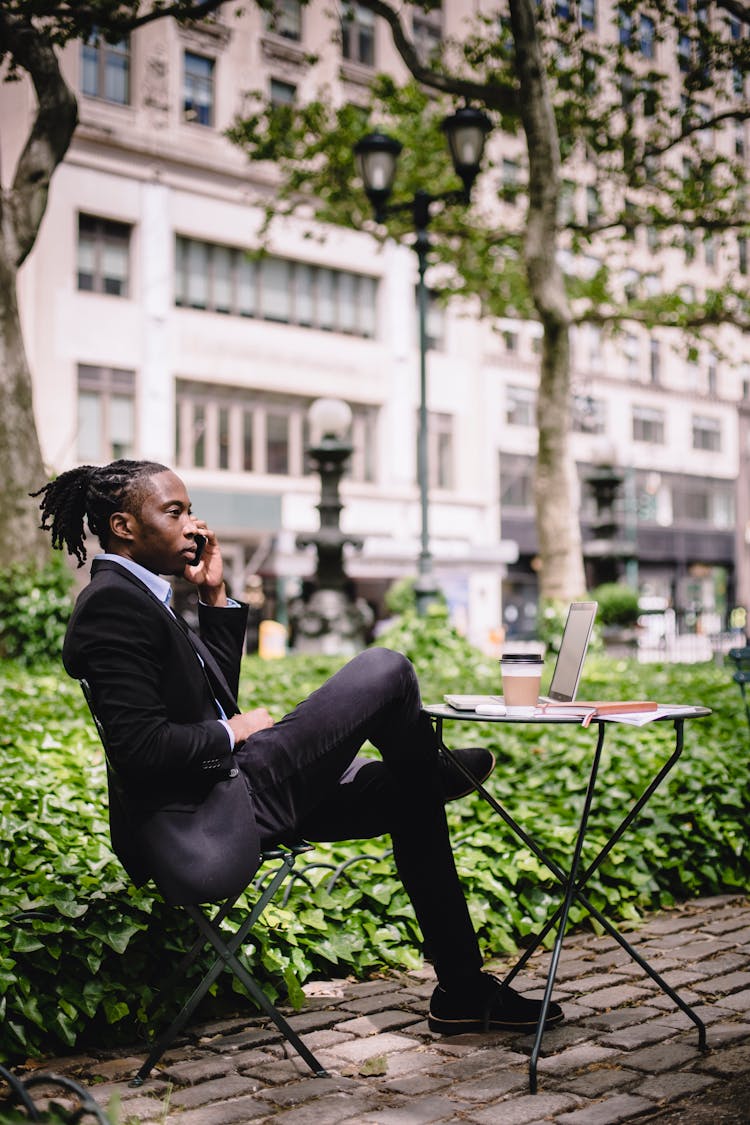 Confident Black Man Talking On Smartphone During Remote Work In Cafe