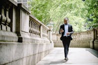 一名穿着西装的年轻非裔美国男子在城市公园的人行道上边走边看手机