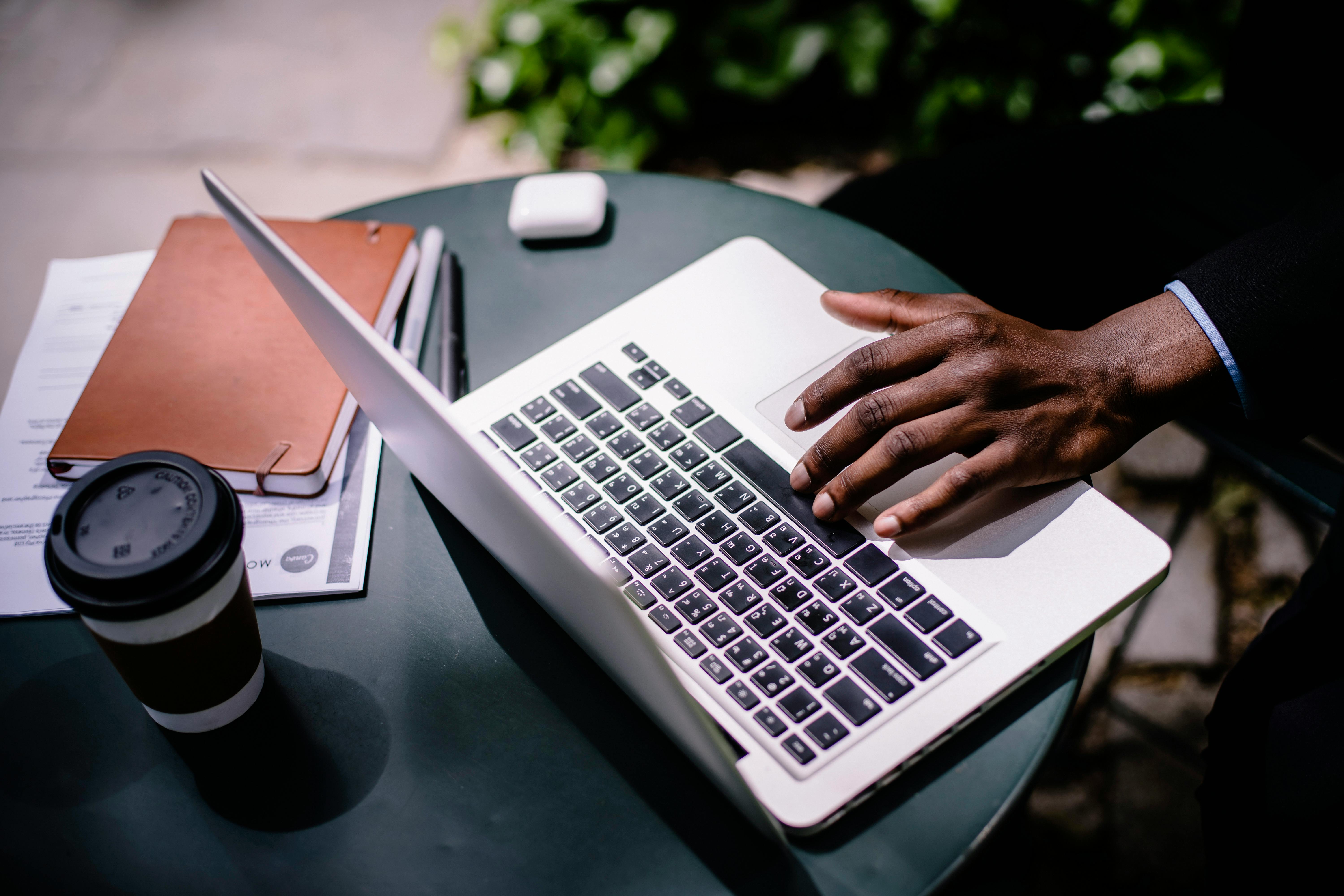 crop unrecognizable black businessman typing on laptop in street cafe