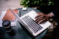 一名商人在户外咖啡桌旁使用笔记本电脑，旁边放着咖啡和文件