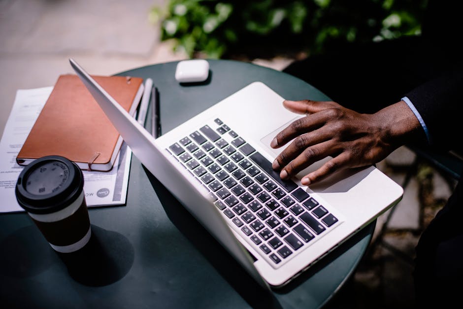 Crop unrecognizable black businessman typing on laptop in street cafe