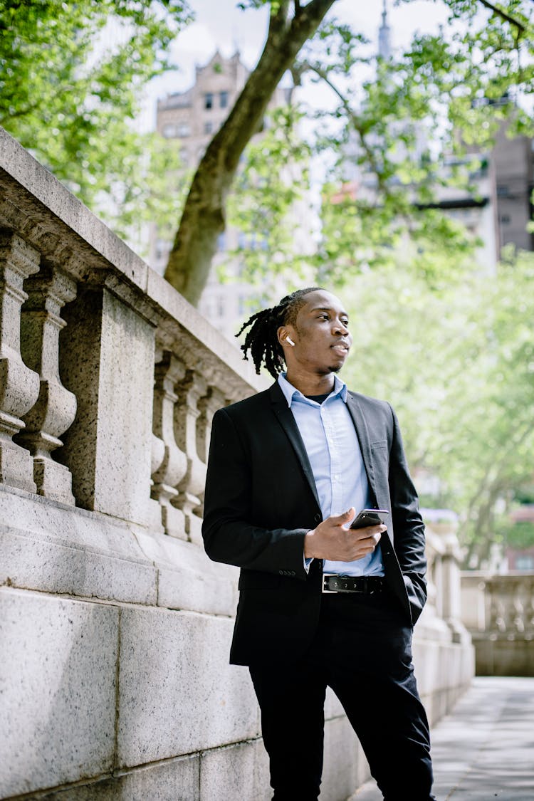 Stylish Young Black Man With Smartphone Standing On Sidewalk In Downtown