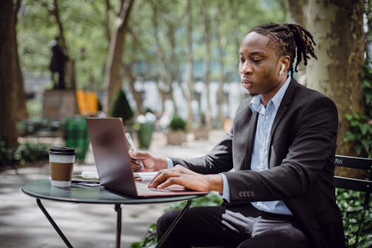Young man focused on work with laptop outdoors in a park setting.