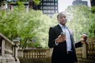 Positive young black man with smartphone and takeaway coffee in city park