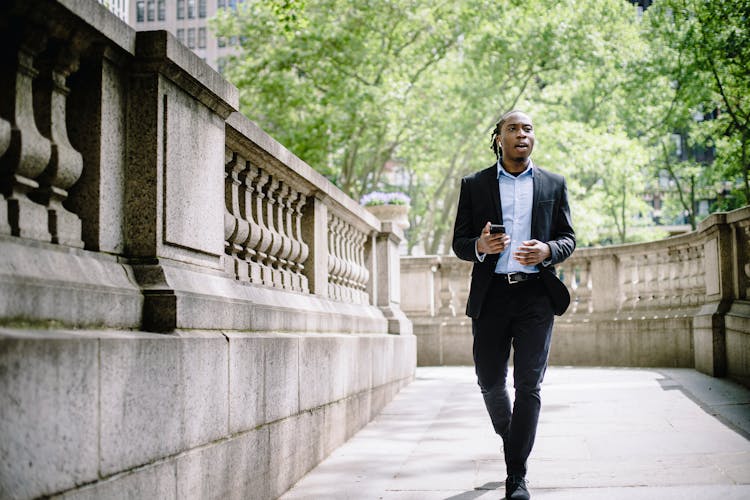 Focused Black Manager Going To Work And Talking On Smartphone Via Wireless Earphones