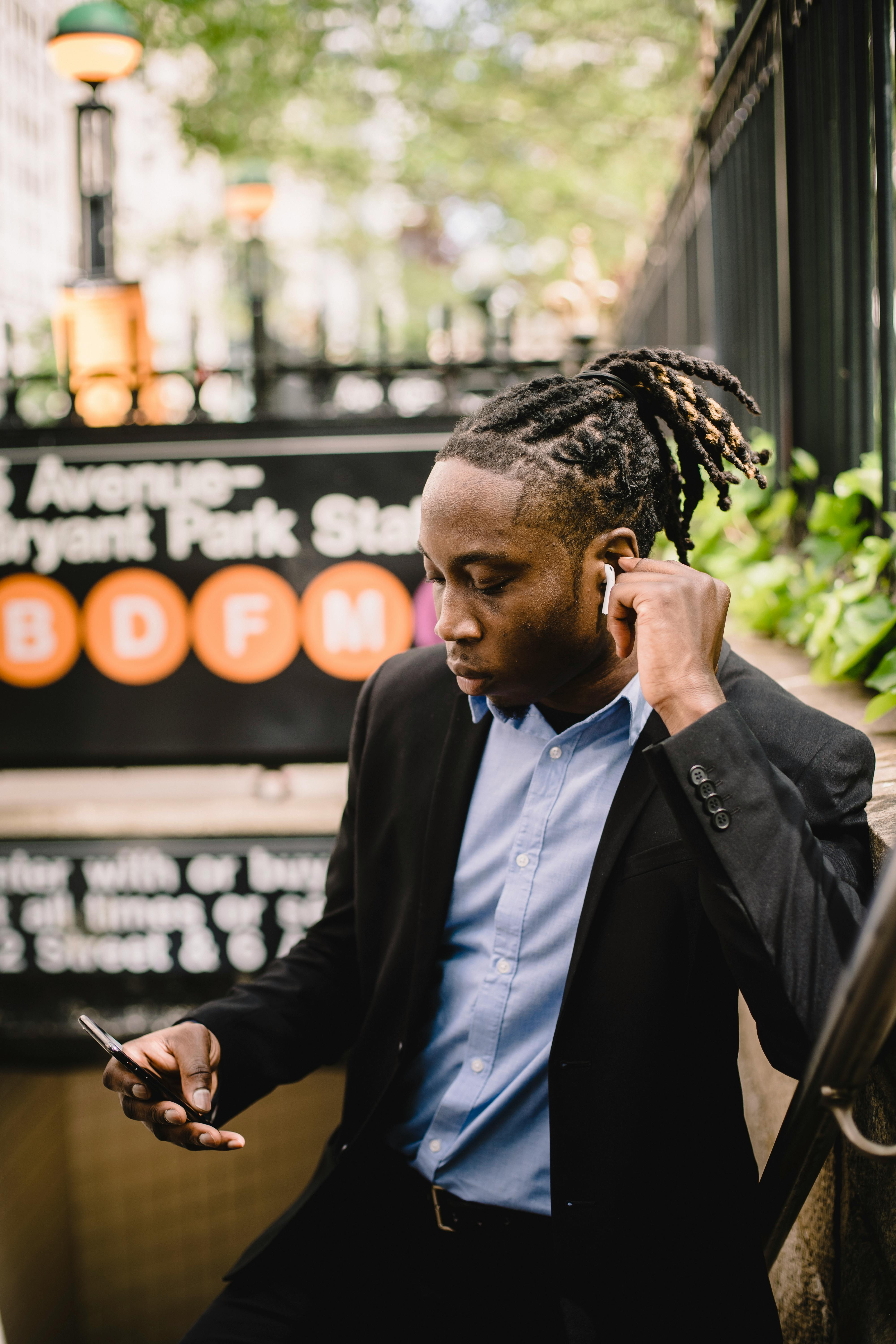 Young professional man with earbuds using phone outside a subway entrance in a city setting.