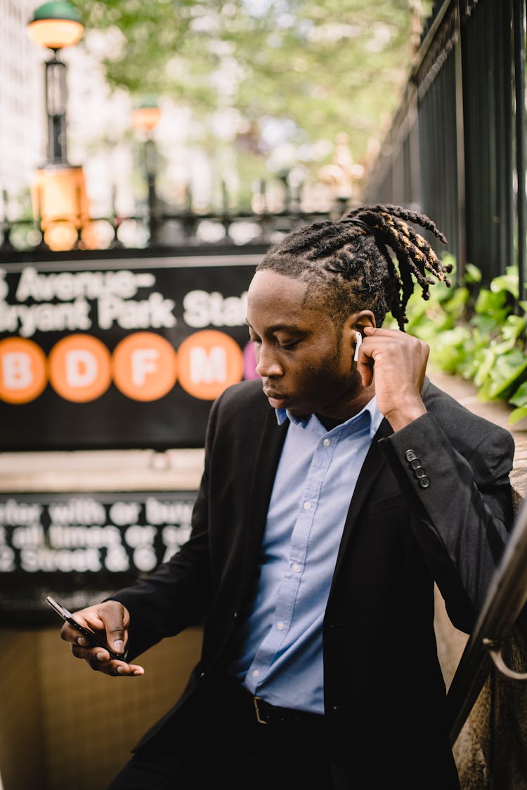 Busy Black Businessman Answering Phone Call Via Wireless Earphones Standing On Stairs Of Subway