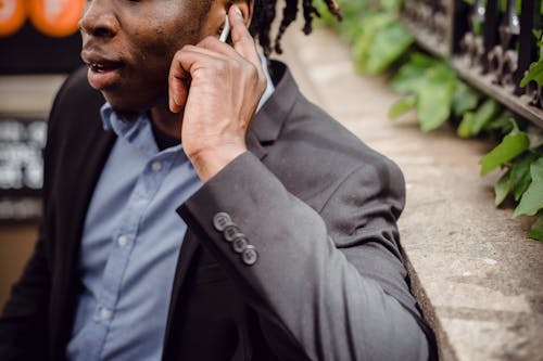 Free Crop well dressed black busy male having phone conversation and listening to interlocutor through wireless earbuds on street on summer day Stock Photo