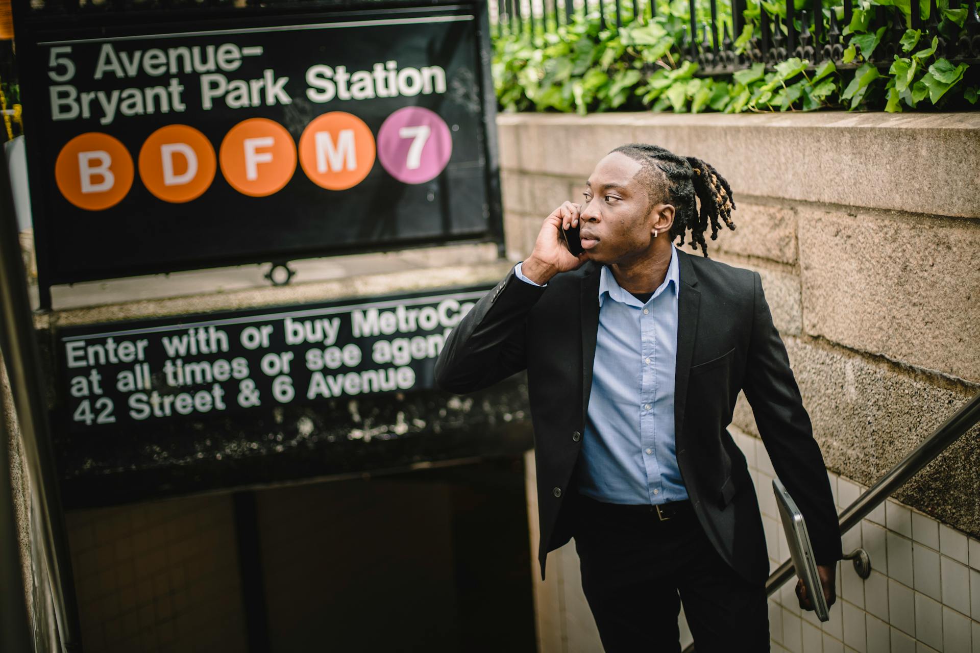 Young black office worker in smart suit with dreadlocks talking on cellphone while exiting subway on summer day in New York